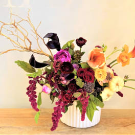 Mixed floral arrangement in a white vase with branches and dark blooms