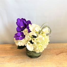 Purple orchids and white calla lilies arranged in a glass vase
