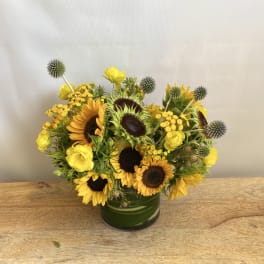 Yellow sunflowers and roses arranged in a green glass vase