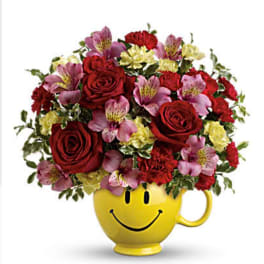 Bouquet of red roses, pink alstroemeria, and carnations in a yellow smiley-face mug