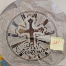 Round decorative plaque with a cross and the words First Communion