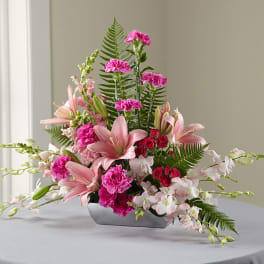Pink lilies, carnations, and orchids in a low silver vase