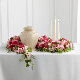 Pink rose arrangement around a beige urn with three lit taper candles