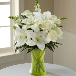 White lilies and roses in a green glass vase