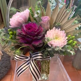 Pink and magenta floral arrangement in a clear glass vase with a striped ribbon