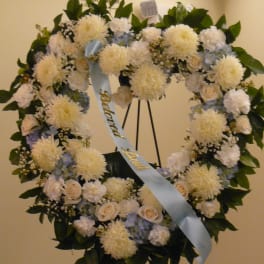 Heart-shaped funeral wreath with white flowers and a blue ribbon on an easel