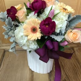 Bouquet of mixed flowers in a white vase with a purple ribbon