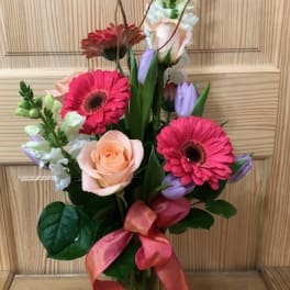 Mixed bouquet with pink gerberas, a peach rose, and purple tulips in a glass vase