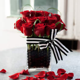 Red roses arranged in a clear square vase with a striped ribbon
