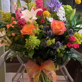Bright mixed bouquet with orange roses, white lilies, and pink blooms in a clear vase with an orange bow