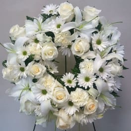 White floral wreath with roses, lilies, and daisies on a stand