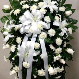 White funeral spray with lilies, mums, and ribbon on an easel
