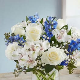 White roses and blue flowers arranged in a clear glass vase