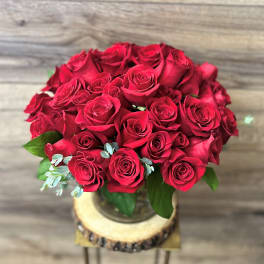 Bouquet of red roses in a glass vase on a wood slice stand