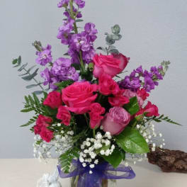 Pink and purple rose bouquet in a glass vase with a purple ribbon