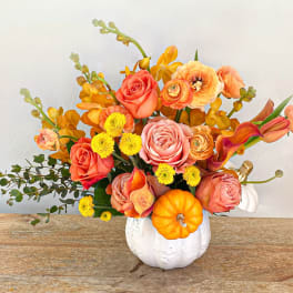 Orange and pink floral arrangement in a white pumpkin vase