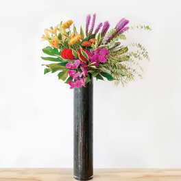 Tropical bouquet with orchids and orange blooms in a tall black vase