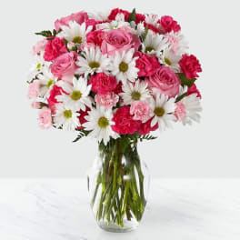 Pink roses, white daisies, and pink carnations arranged in a clear glass vase