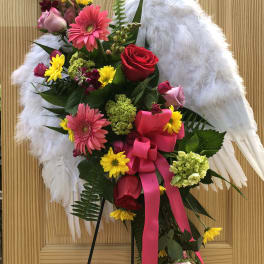 Floral standing spray with pink and red roses, gerbera daisies, and white wings