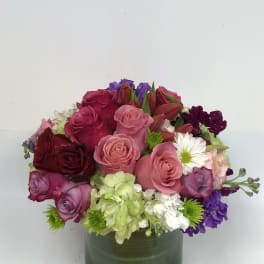Mixed bouquet of roses, lilies, and daisies in a green glass vase
