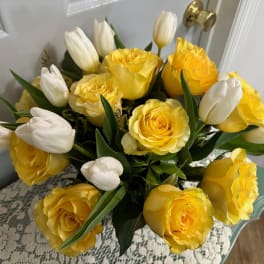 Arrangement of yellow roses and white tulips in a compact round bouquet on a lace-covered table