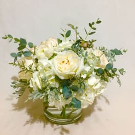 Low white and cream rose and hydrangea arrangement in a clear glass cylinder vase