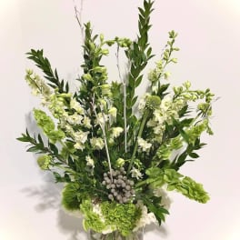 Tall green and white floral arrangement with hydrangeas and bells of Ireland in a clear glass vase.