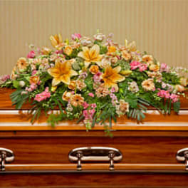 Casket spray of yellow lilies with peach and pink flowers on a polished wood casket