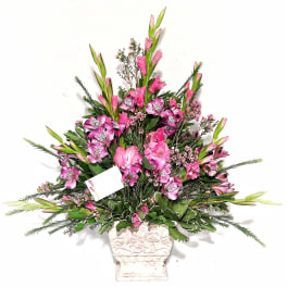 Tall pink floral arrangement in a white urn-style vase with a small card