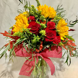 Clear vase arrangement with yellow sunflowers and red roses accented with a large red bow.