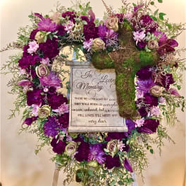 Standing sympathy wreath of purple and cream flowers with a moss-covered cross and memorial plaque on an easel