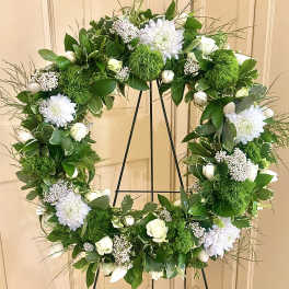 Standing wreath of white flowers and green accents on a metal easel