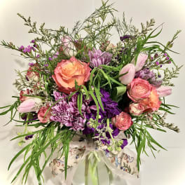 Mixed bouquet of pink roses, purple mums, and tulips with trailing greenery in a glass vase