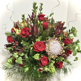 Large arrangement of red roses and king protea in a clear glass vase