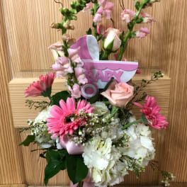 Pink and white floral arrangement in a glass vase with a baby topper