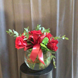 Red roses arranged in a round glass vase with a red ribbon