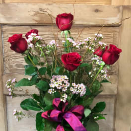 Red roses in a clear glass vase with pink filler flowers and a purple ribbon