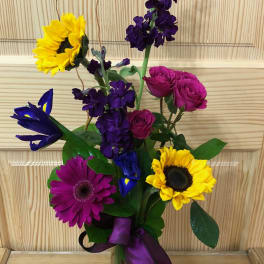 Colorful mixed bouquet in a clear glass vase with a purple ribbon