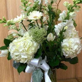 White floral arrangement in a glass vase with a white ribbon