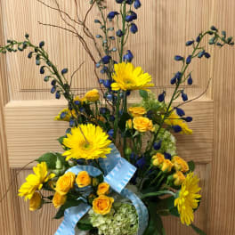 Yellow gerberas and roses in a glass vase with blue ribbon accents