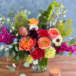 Mixed bouquet of roses and other blooms in a glass vase with a candle nearby