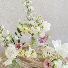Three small floral arrangements in glass vases with white and pink blooms