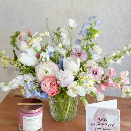 Mixed pastel bouquet in a clear glass vase beside a candle and thank-you card