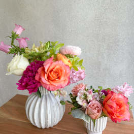 Two colorful floral arrangements in white vases on a wooden table