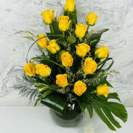 Yellow roses arranged in a glass vase with dark green foliage.