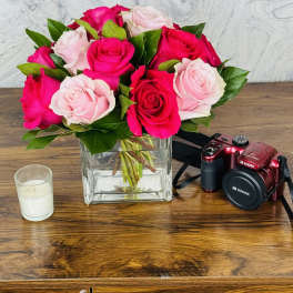 Pink and red roses in a square glass vase on a wooden table