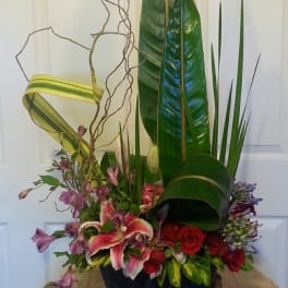 Tall floral arrangement with red roses, pink lilies, and large tropical leaves