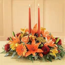 Orange floral centerpiece with two red taper candles