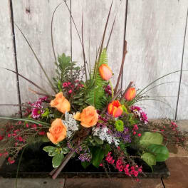 Low floral arrangement with orange roses and tulips in a black container