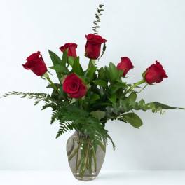 Red roses arranged in a clear glass vase with greenery